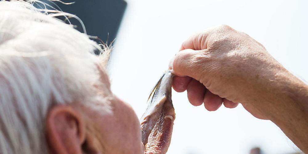ARCHIV - Ein Besucher der Emder Matjestage isst einen Matjes. Foto: Mohssen Assanimoghaddam/dpa