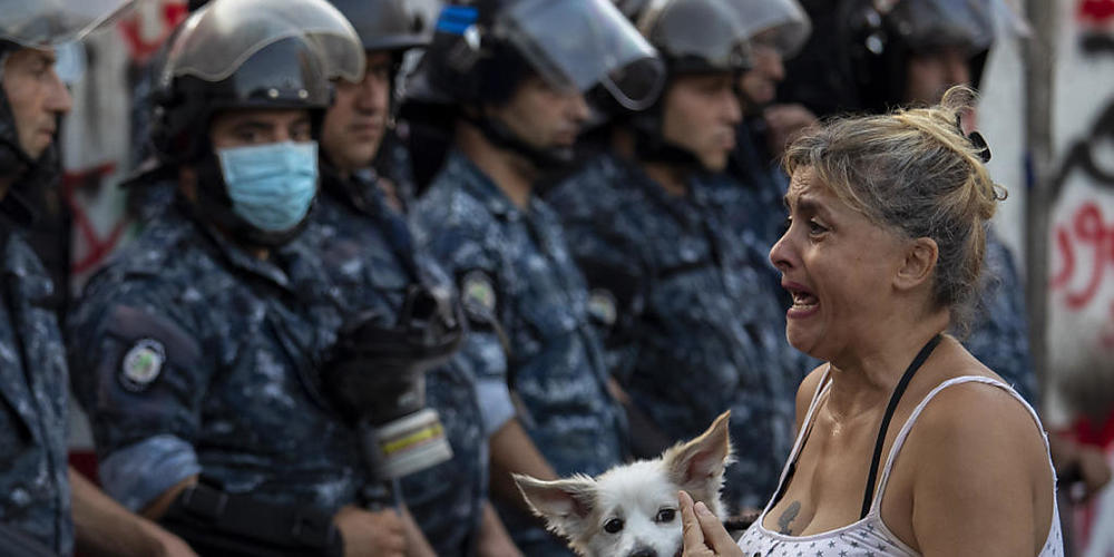 Eine Teilnehmerin eines regierungskritischen Protestes vor einer Kette Polizisten. Foto: Hassan Ammar/AP/dpa