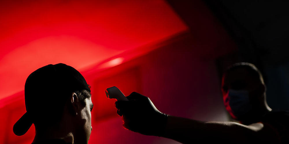 Ein Sicherheitsmitarbeiter misst einem Gast in einem Club die Temperatur. (Symbolbild)