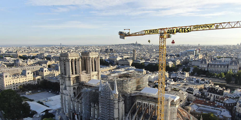 HANDOUT - Ein Transparent: "Klima. In Aktion" ist an einem Kran an der Baustelle der Kathedrale Notre Dame befestigt. Mit einer Aktion auf der Baustelle der Kathedrale Notre-Dame hat die Umweltschutzorganisation Greenpeace in Paris für Aufsehen ge...