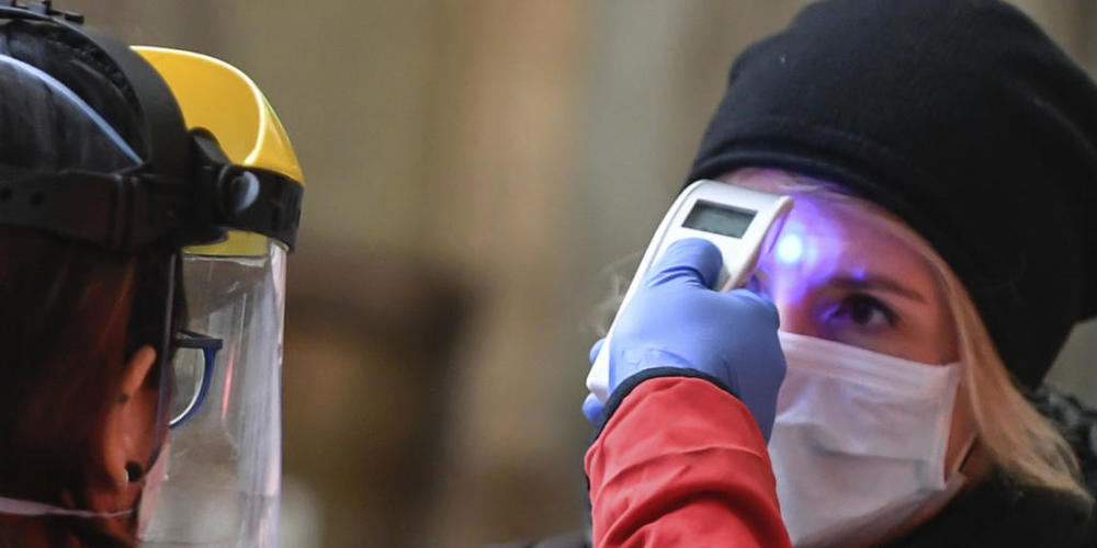 ARCHIV - Eine Mitarbeiterin des Roten Kreuzes überprüft auf dem Hauptbahnhof am Zugangsbereich für Zugabfahrten die Temperatur einer Frau. (zu dpa «Anstieg bei Corona-Zahlen: Italien prüft Zwangseinweisung von Kranken») Foto: Claudio Furlan/LaPres...