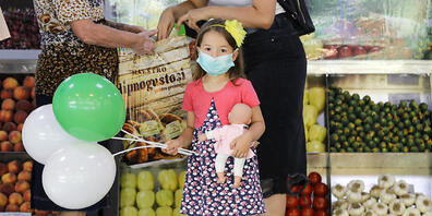 Ein Mädchen mit medizinischem Mundschutz hält Luftballons und eine Puppe in einem Lebensmittelmarkt in Bukarest. Rumänien verzeichnet einen Rekord an Neuinfektionen mit dem Coronavirus. Foto: Vadim Ghirda/AP/dpa