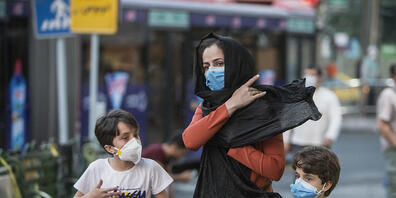 Kinder mit Gesichtsmasken gehen mit ihrer Mutter eine Straße entlang. Der Iran meldete am 21. Juli eine neue Rekordzahl an Corona-Toten. Foto: Ahmad Halabisaz/XinHua/dpa