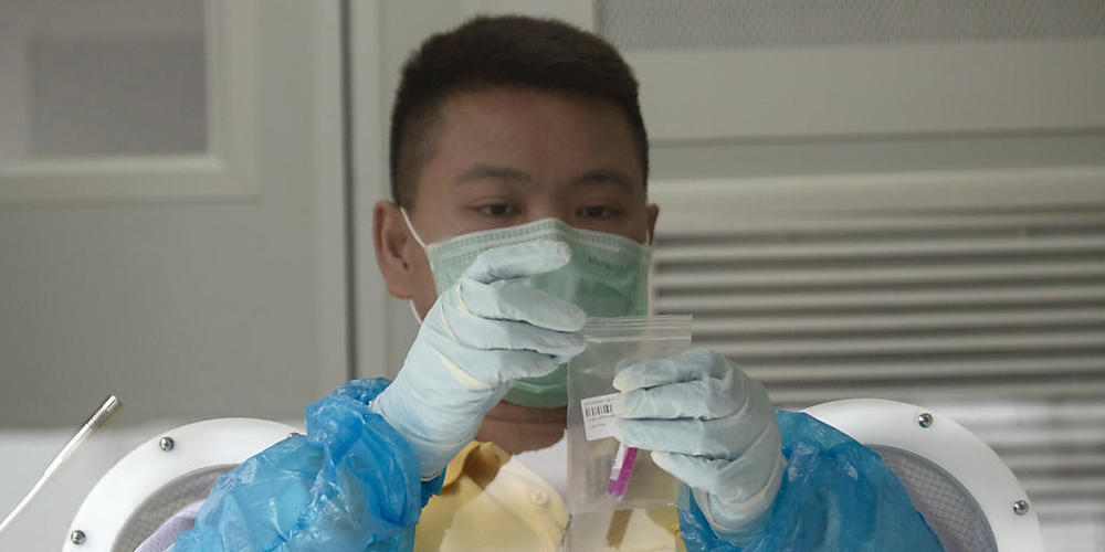 Ein Mitarbeiter des Gesundheitswesens verschließt die Probe eines Nasenabstrichs, den er zuvor einer Patientin, die einen Corona-Test hat durchführen lassen, entnommen hat. Foto: Sakchai Lalit/AP/dpa