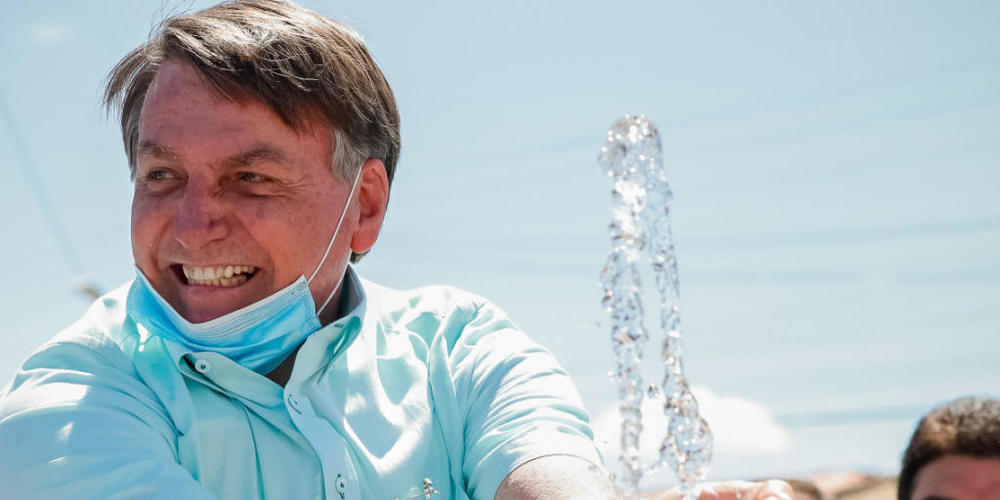 HANDOUT - Auf diesem vom brasilianischen Präsidentenamt zur Verfügung gestellten Bild lächelt Jair Bolsonaro, Präsident von Brasilien, mit untergezogenem Mundschutz, während er an einem Brunnen zur lokalen Wasserversorgung mit Wasser spielt. Foto:...