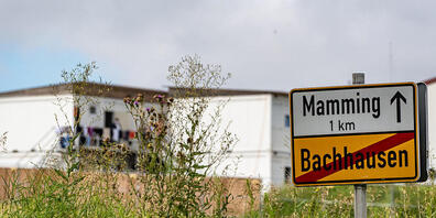 Das Ortsschild von Mamming, im Hintergrund sind die Unterkünfte von Erntehelfern zu sehen. Foto: Armin Weigel/dpa