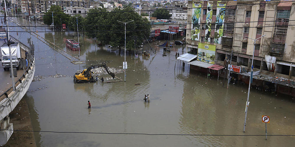 Menschen waten durch ein überschwemmtes Gebiet nach einem starken Regenfall in Karatschi. Foto: Fareed Khan/AP/dpa