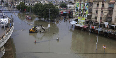Menschen waten durch ein überschwemmtes Gebiet nach einem starken Regenfall in Karatschi. Foto: Fareed Khan/AP/dpa