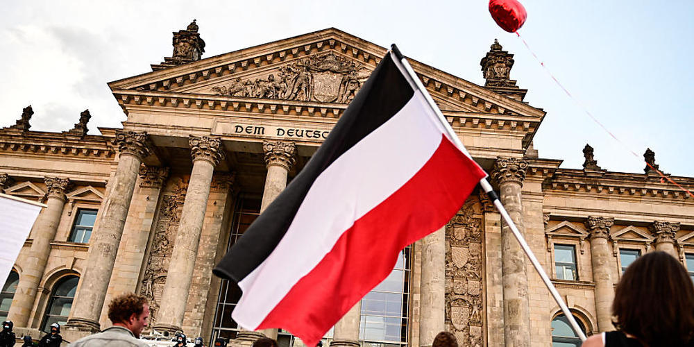 Teilnehmer einer Kundgebung gegen die Corona-Maßnahmen stehen vor dem Reichstag, ein Teilnehmer hält eine Reichsflagge. Foto: Fabian Sommer/dpa