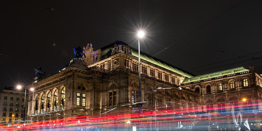 ARCHIV - Die Lichter vorbeifahrender Autos sind vor der Wiener Staatsoper am Abend zu sehen (Langzeitbelichtung). Die Wiener Staatsoper wird am 7. September mit der Premiere von «Madama Butterfly» ihren seit sechs Monaten wegen der Corona-Krise un...
