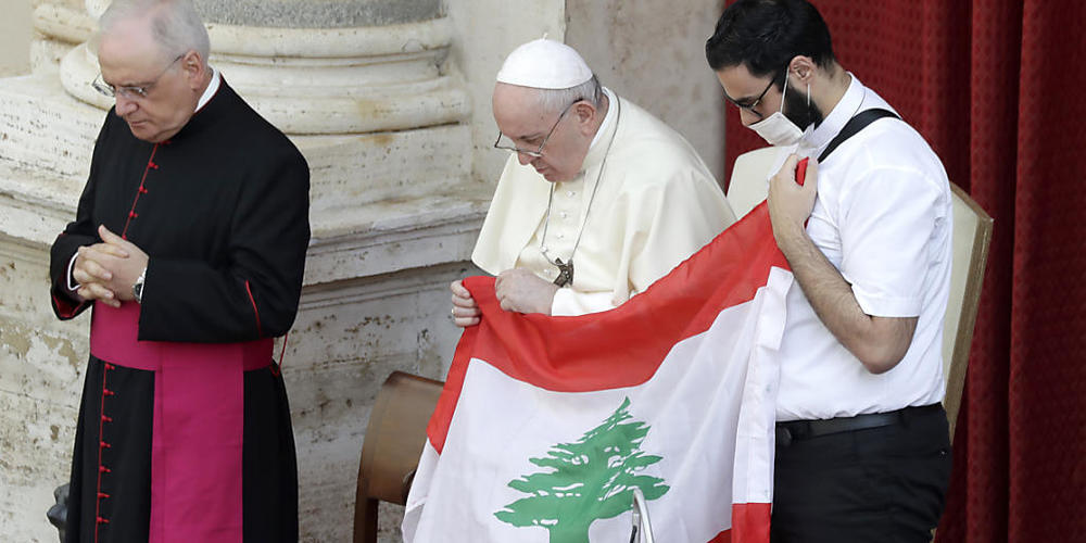 Papst Franziskus (M) hält bei seiner ersten Generalaudienz mit Gläubigen seit Ausbruch der Corona-Pandemie in Gedenken an die Opfer der Explosion die Flagge des Libanon. Foto: Andrew Medichini/AP/dpa