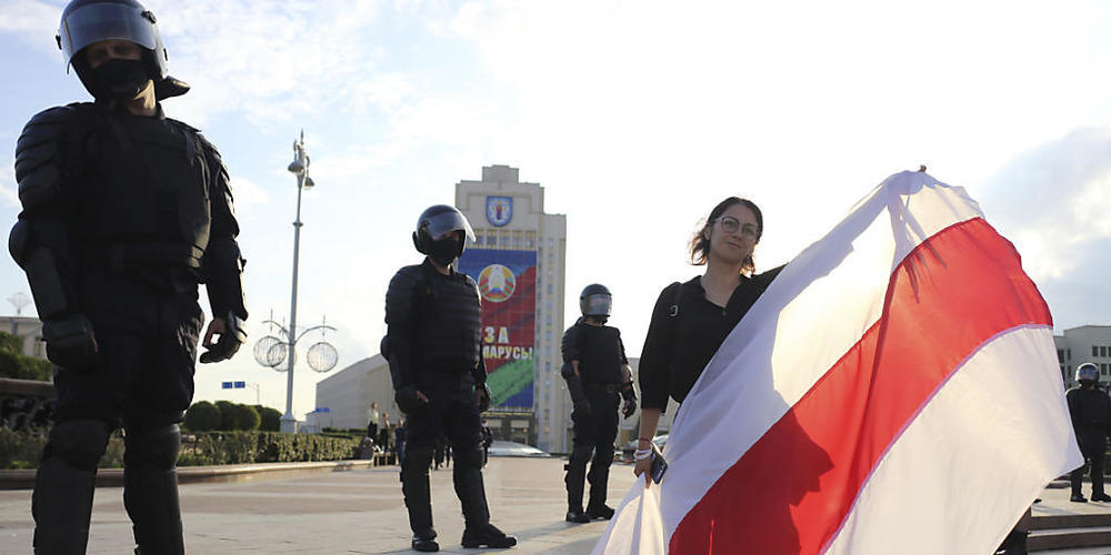 Eine Demonstrantin und Bereitschaftspolizisten stehen auf dem Unabhängigkeitsplatz in Minsk. Foto: -/AP/dpa