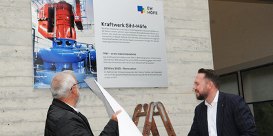 Projektleiter Arnold Nölly und Diego Föllmi enthüllen die neue Infotafel am Kraftwerkgebäude. (Bild: Frieda Suter)