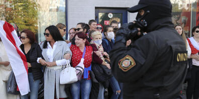 Frauen mit alten belarussischen Nationalflaggen stehen bei einer Demonstration gegen die Wahlergebnisse in Belarus neben einem Polizeibeamten. Foto: Uncredited/TUT.by/dpa