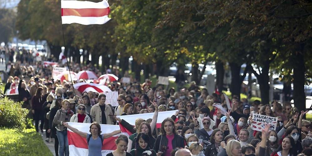 Frauen mit alten belarussischen Nationalflaggen gehen bei einer Demonstration gegen die Wahlergebnisse in Belarus über eine Straße. Foto: Uncredited/TUT.by/dpa
