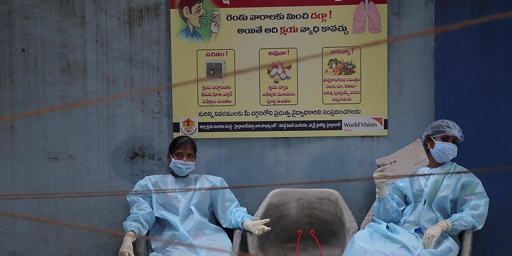 Medizinische Mitarbeiterinnen in Schutzausrüstung ruhen sich vor der Entnahme von Speichelproben für Covid-19-Tests aus. Foto: Mahesh Kumar A/AP/dpa