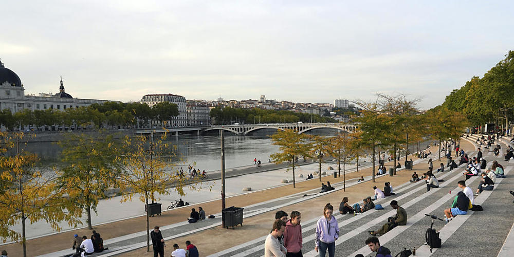 Menschen sitzen entlang des Flusses Rhone. Die französischen Behörden haben die Stadt Lyon auf die höchste Warnstufe gesetzt. Versammlungen sind untersagt und Bars werden schließen müssen. Foto: Laurent Cipriani/AP/dpa
