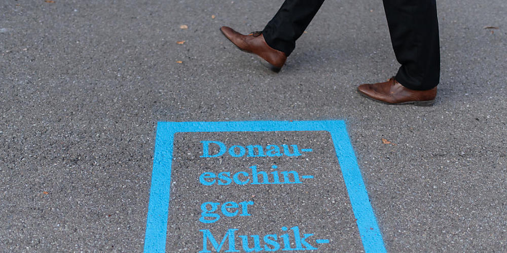ARCHIV - Ein Mann läuft am Logo der Donaueschinger Musiktage vor der Donauhalle vorbei. Die Donaueschinger Musiktage sind nach Angaben der Veranstalter das weltweit älteste und renommierteste Festival für Neue Musik. Foto: Patrick Seeger/dpa
