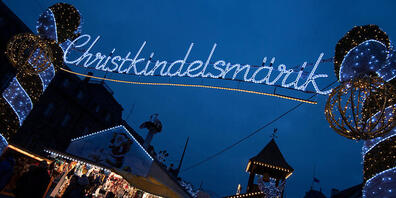 ARCHIV - Das Wort "Christkindelsmärik" prangt in großen beleuchteten Buchstaben an einem Zugang zum Weihnachtsmarkt. Foto: Marijan Murat/dpa