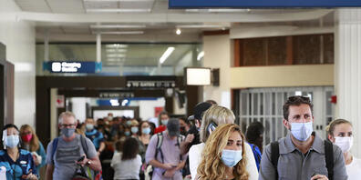 Reisende an einem Flughafen auf Hawaii tragen Mund-Nasen-Schutz. Foto: Marco Garcia/AP/dpa