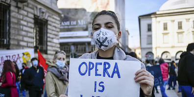 Eine Frau mit Mundschutz hält bei einer Demonstration gegen die Maßnahmen der Regierung zur Eindämmung der Corona-Pandemie ein Schild mit der Aufschrift «Opera is work» (zu deutsch: «Oper ist Arbeit») in den Händen. Foto: Claudio Furlan/LaPresse/A...