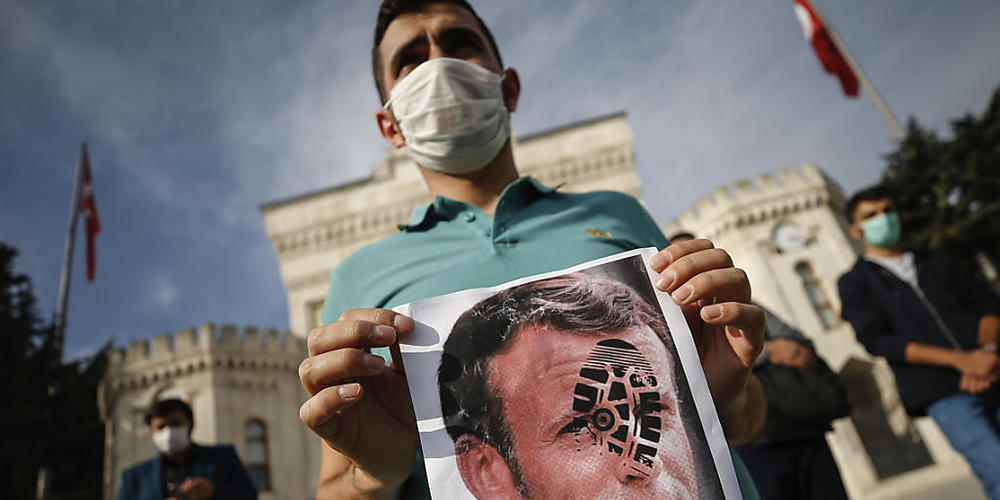 Ein junger Mann hält in Istanbul ein mit einem Schuhabdruck versehenes Foto von Emmanuel Macron in die Kamera. Foto: Emrah Gurel/AP/dpa