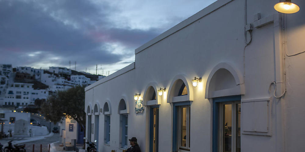 Ein Mann sitzt allein auf einem Stuhl vor einem Restaurant auf der Insel Astypalea. Foto: Petros Giannakouris/AP/dpa