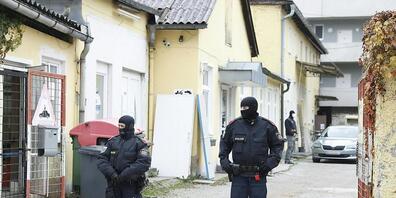 Zwei Polizisten stehen in einer Einfahrt an einem Einsatzort der Operation «Luxor» in Graz. Foto: Erwin Scheriau/APA/dpa - ACHTUNG: Die Kfz-Kennzeichen wurden aus persönlichkeitsrechtlichen Gründen gepixelt.