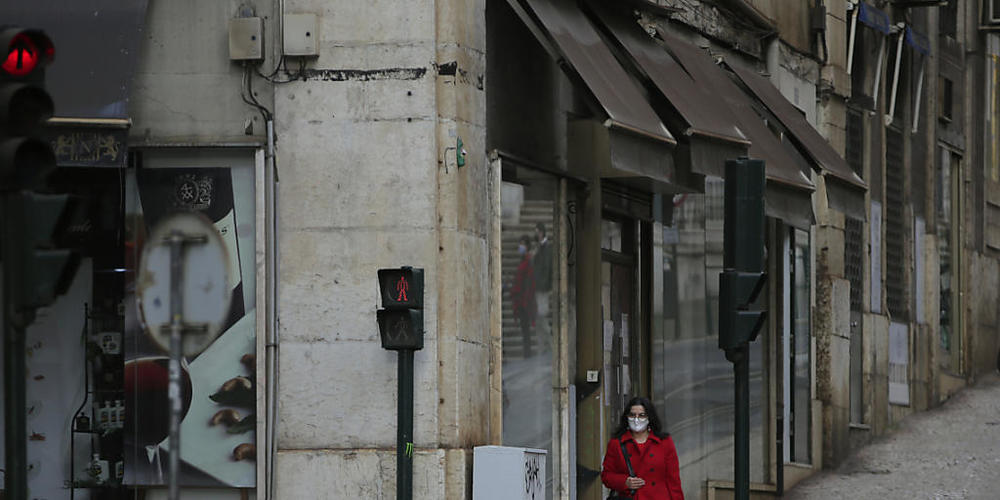 ARCHIV - Eine Frau mit Maske geht eine sehr ruhige Straße in der Innenstadt entlang. Foto: Armando Franca/AP/dpa