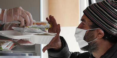 dpatopbilder - Ein Freiwilliger reicht einem Obdachlosen mit Mund-Nasen-Schutz Essen. Landesweit in Italien sind verschärfte Corona-Schutzvorschriften in Kraft getreten. Foto: Antonio Calanni/AP/dpa