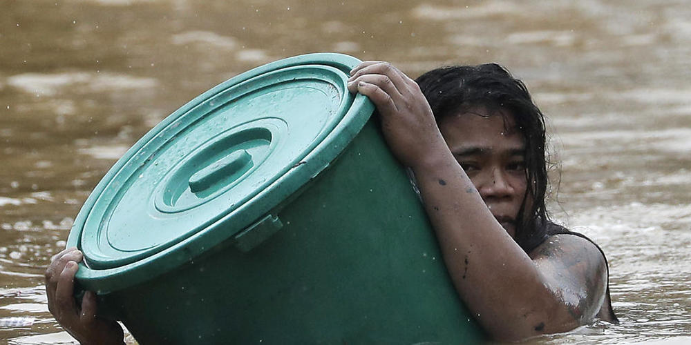 Eine Anwohnerin hält sich an einen Plastikbehälter als Schwimmboje fest, während sie in dem steigenden Hochwasser schwimmt. Foto: Aaron Favila/AP/dpa
