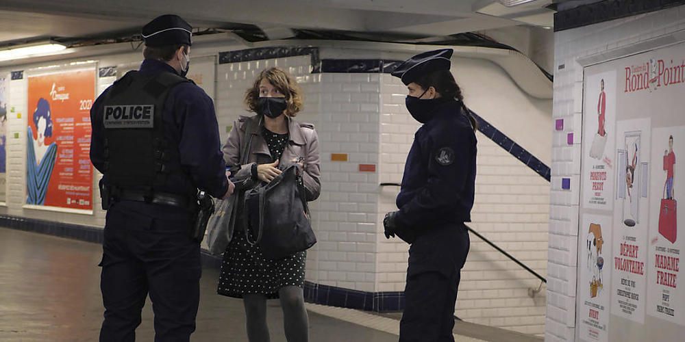 In einer U-Bahn-Station in Paris kontrollieren zwei Polizisten eine Pendlerin. Im Kampf gegen die Corona-Pandemie gelten in Frankreich weitreichende Ausgangsbeschränkungen. Foto: Thibault Camus/AP/dpa