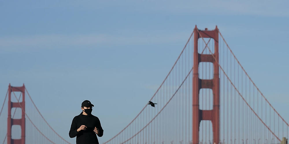 Eine Frau mit Mund-Nasen-Schutz läuft auf einem Weg vor der Golden Gate Bridge. Foto: Jeff Chiu/AP/dpa