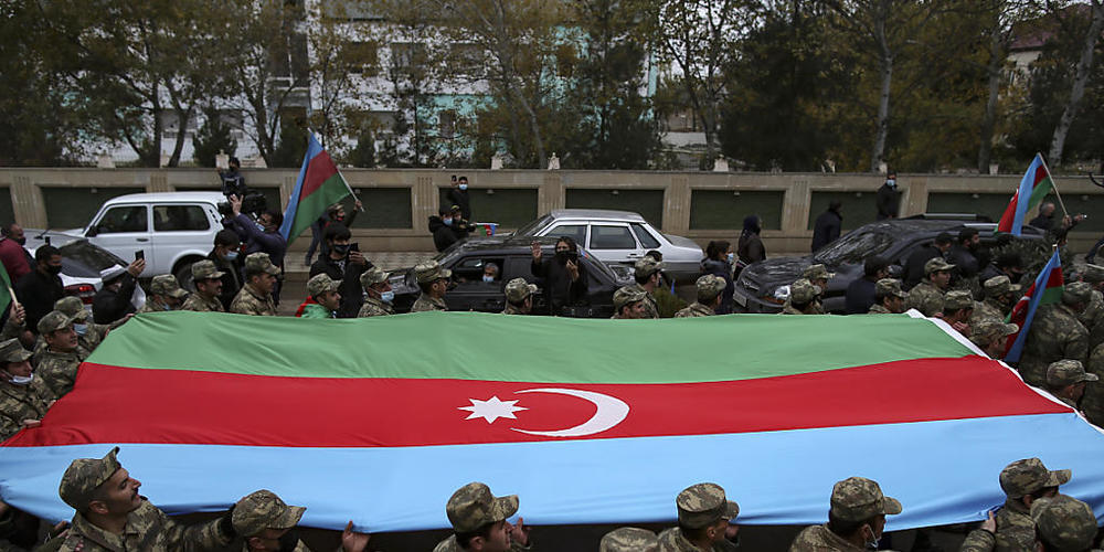 Aserbaidschanische Soldaten tragen eine große Fahne in den Farben ihrer Nationalflagge, während sie die Rückgabe der Region Latschin feiern. Foto: Emrah Gurel/AP/dpa