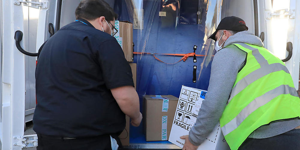 Ein Apothekentechniker des Gesundheitsdienstes von Croydon (l) nimmt im Universitätskrankenhaus Croydon die erste Charge der Covid-19-Impfungen entgegen, die in das Gebiet geliefert werden sollen. Foto: Gareth Fuller/PA Wire/dpa
