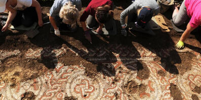 HANDOUT - Archäologen legen ein Mosaik frei, das bei Ausgrabungsarbeiten des National Trust an einer römischen Villa in Chedworth entdeckt wurde. Foto: National Trust/PA Media/dpa - ACHTUNG: Nur zur redaktionellen Verwendung im Zusammenhang mit de...
