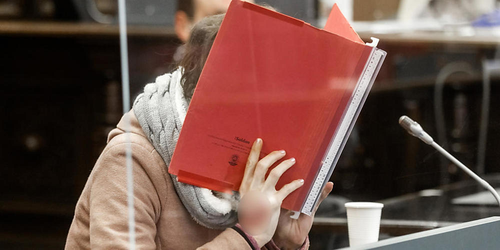 Die 37-jährige Angeklagte sitzt im Gerichtssaal und verbirgt ihr Gesicht hinter einer Akte. Foto: Markus Scholz/dpa Pool/dpa - ACHTUNG: Ein Tattoo auf der Hand wurde aus rechtlichen Gründen gepixelt