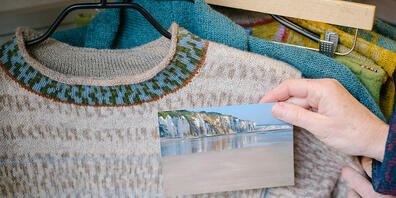 Die Textildesignerin Anne-Susanne Gueler hält in ihrem Werkstattladen "hand-werk" ein Foto aus der Normandie neben einen von ihr gestrickten Pullover. Gueler lässt sich häufig von Landschaften inspirieren. Foto: Ole Spata/dpa