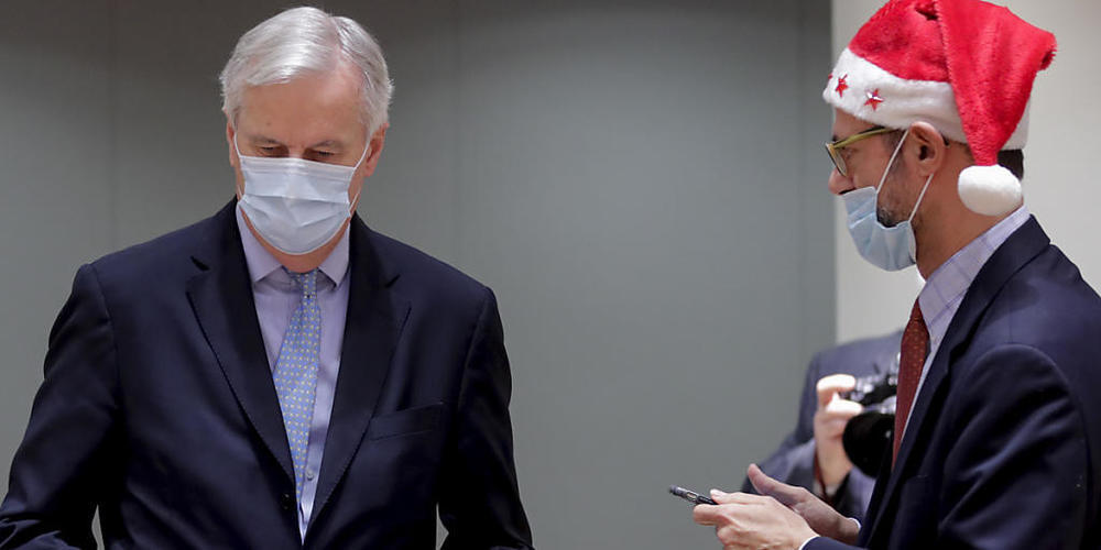 dpatopbilder - Michel Barnier (l), EU-Chefunterhändler für den Brexit aus Frankreich, trägt einen Ordner mit dem Brexit-Handelsabkommen neben einem Kollegen, der eine Weihnachtsmannmütze trägt, während einer Sondersitzung im EU-Hauptquatier. Foto:...