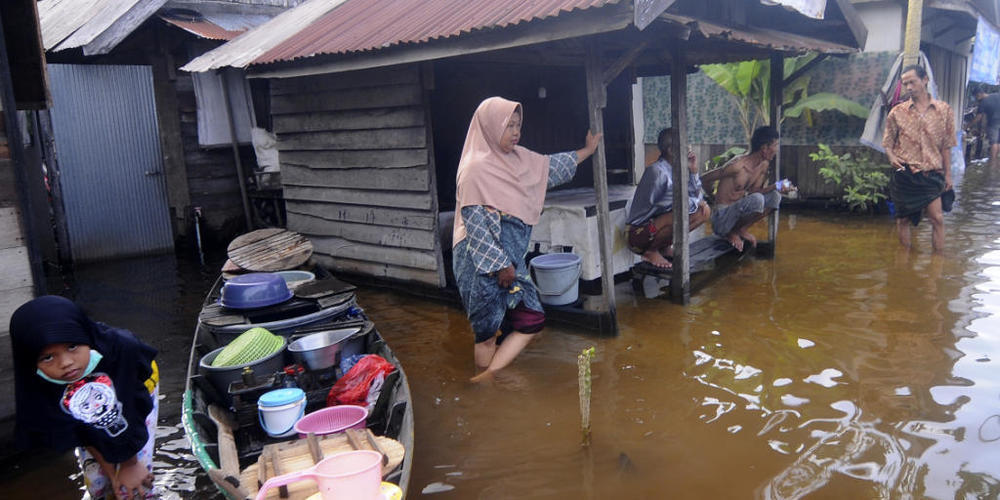 Anwohner stehen auf der überfluteten Straße vor ihren Häusern auf der indonesischen Insel Borneo. Foto: Iman Satria/AP/dpa