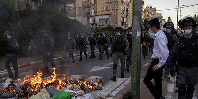 Polizisten gehen während einer Demonstration von ultraorthodoxen Juden auf einer Straße an brennendem Müll vorbei. Foto: Oded Balilty/AP/dpa