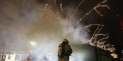 Krawalle in Rotterdam: Ein Feuerwehrmann löscht einen Container, der bei Protesten gegen eine landesweite Ausgangssperre in Brand gesetzt wurde. Foto: Peter Dejong/AP/dpa