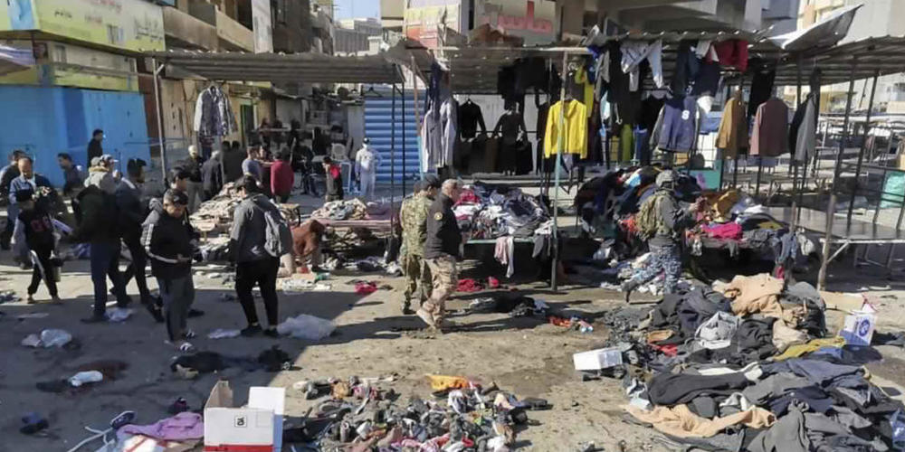 Menschen und Sicherheitskräfte gehen in der irakischen Hauptstadt am Ort eines tödlichen Anschlags, einem Markt, auf dem gebrauchte Kleidung verkauft wurde, an auf dem Boden verstreuten Kleidung und Schuhen vorbei. Foto: Hadi Mizban/AP/dpa