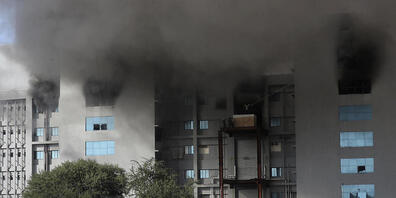 dpatopbilder - Mitarbeiter verlassen ein Gebäude des «Serum Institute of India», dem weltgrößten Impfstoffproduzenten in Indien, aus dem Rauch aus Fensteröffnungen quillt. Foto: Rafiq Maqbool/AP/dpa