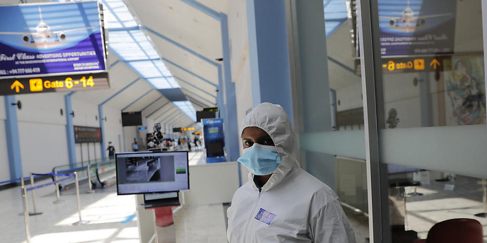 Ein Flughafenmitarbeiter im Schutzanzug und mit Mund-Nasen-Bedeckung steht neben einem Temperaturscanner in einem Terminal am Katunayake International Airport. Foto: Eranga Jayawardena/AP/dpa