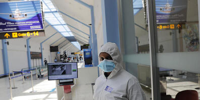 Ein Flughafenmitarbeiter im Schutzanzug und mit Mund-Nasen-Bedeckung steht neben einem Temperaturscanner in einem Terminal am Katunayake International Airport. Foto: Eranga Jayawardena/AP/dpa