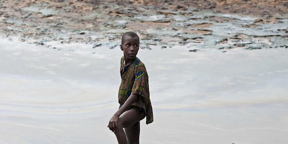 ARCHIV - Ein Jung steht mit seinem Fischernetz am ölverschmierten Ufer eines Baches in der Nähe von Goi in Ogoniland. (zu dpa «Urteil im Prozess gegen Shell wegen Verschmutzung in Nigeria») Foto: Marten Van Dijl/ANP/dpa