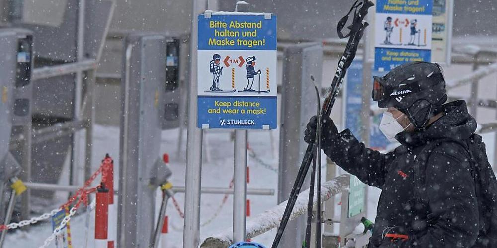Skifahrer stehen vor einer Corona-Schleuse mit den Hinweisen, Abstand zu halten und eine Maske zu tragen, an einem Skilift im Skigebiet "Stuhleck" am Semmering in Niederösterreich. Foto: Herbert Pfarrhofer/APA/dpa