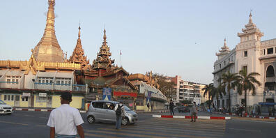 Passanten überqueren eine Straße in der Nähe der Sule-Pagode in Rangun. In Myanmar hat das Militär die Macht übernommen. Foto: Thein Zaw/AP/dpa