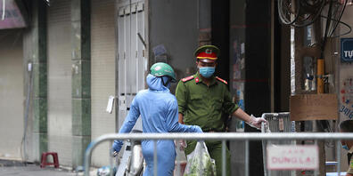 ARCHIV - Eine Frau geht vor einem Supermarkt in Hanoi an einem Polizisten mit Mundschutz vorbei. Foto: Hau Dinh/AP/dpa